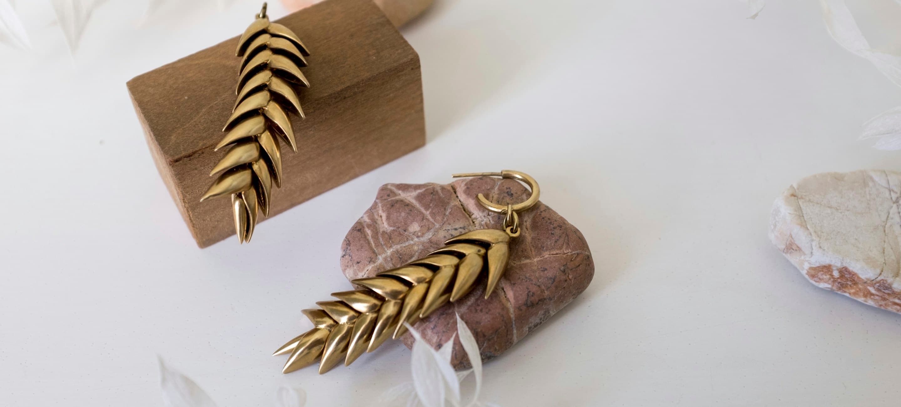Brass leaf drop earrings resting on a wooden block and stone